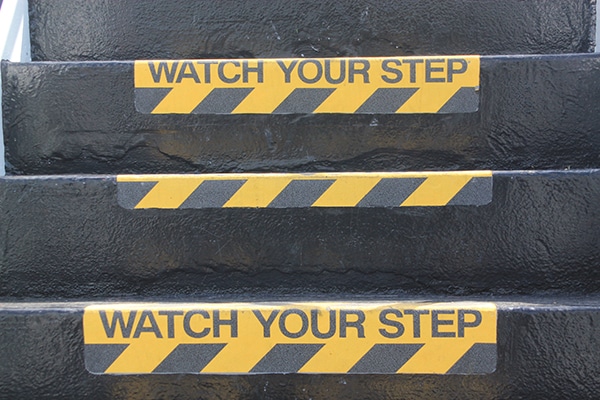 Yellow and black warning sign on stairs stating "Watch your Step", signifying a potential trip hazard.
