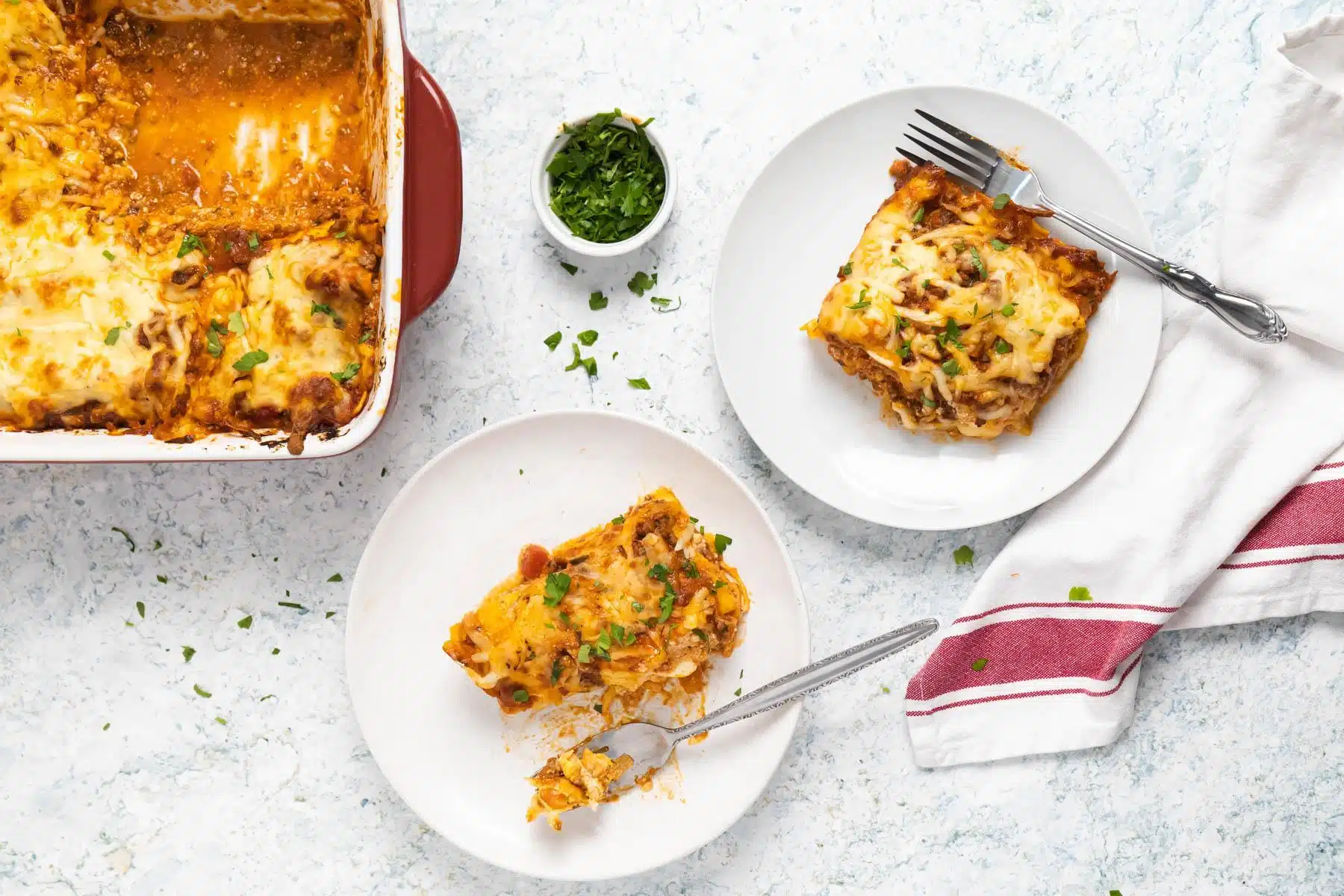 Lasagna pan on a white table with a slice of lasagna on a plate.