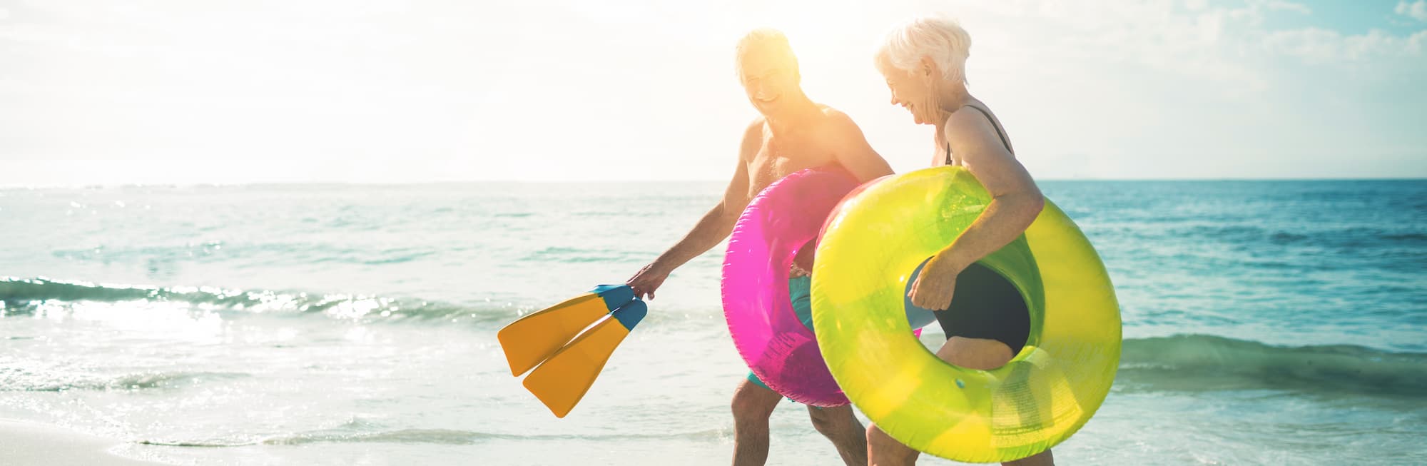 A couple walking on a beach with pool floaties