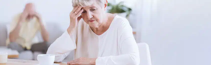 Older woman holds her head sitting at the table. Senior mental health