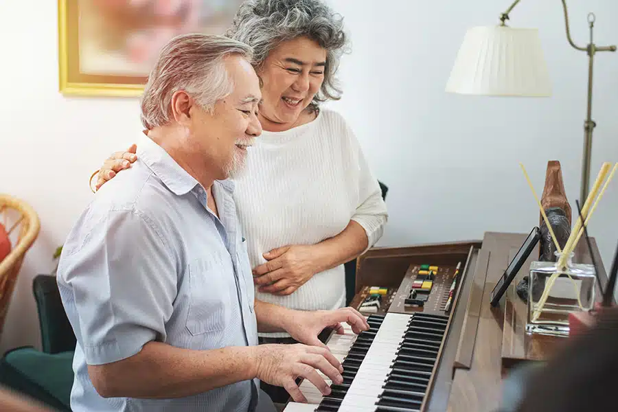 Senior gentleman practices piano in retirement home while woman listens