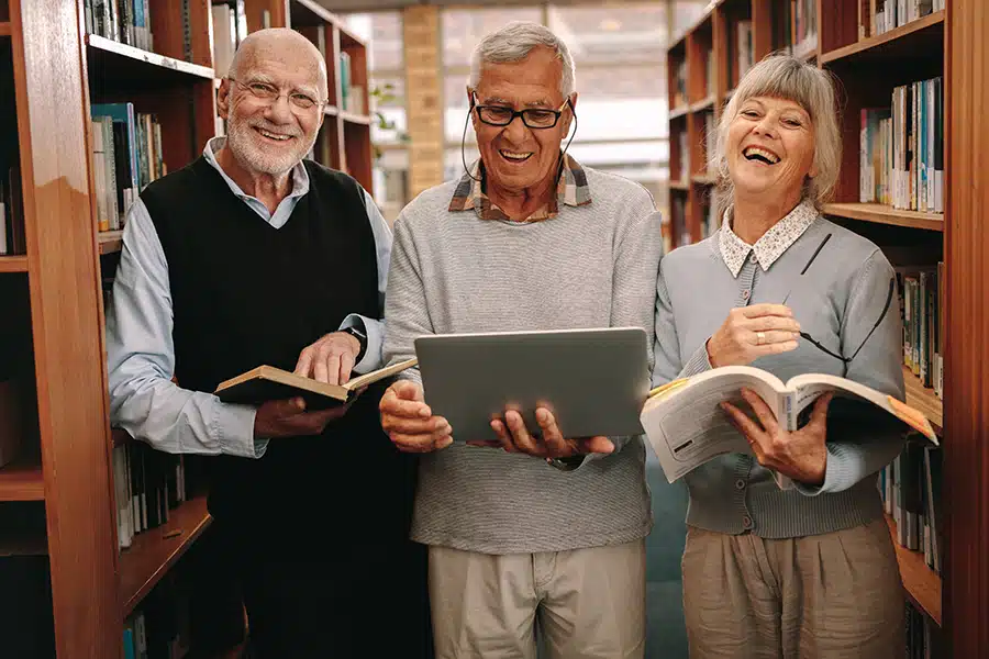 Three happy seniors holding books in the library
