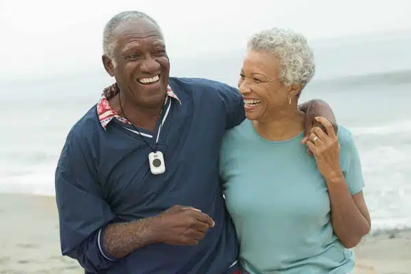 a happy old couple going for a walk on the beach, the man is wearing a carepoint go pendant.