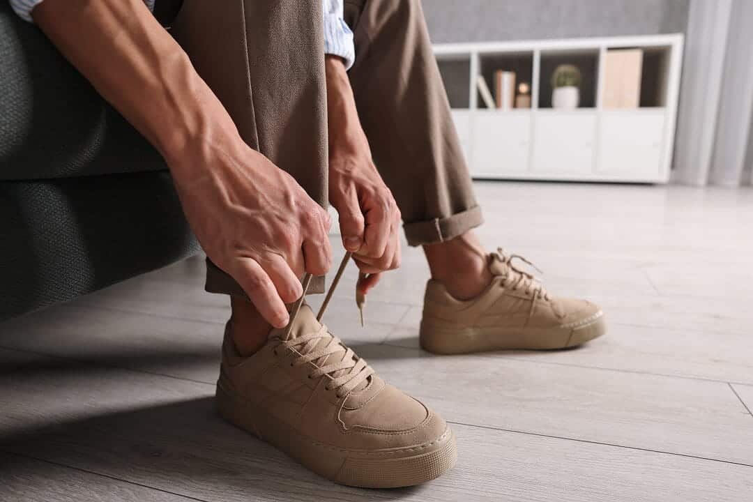 Gros plan sur les mains d'une personne en train de lacer des baskets marron clair, assise à l'intérieur