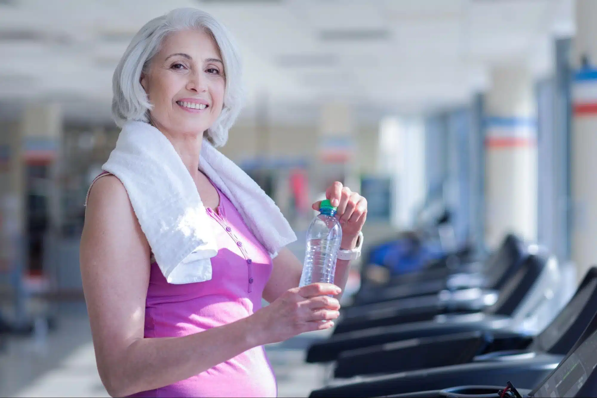 woman holding water while standing on a treadmill