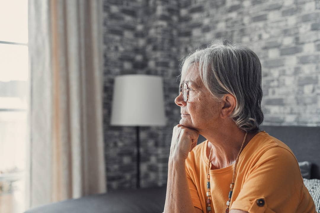 Une personne âgée assise, regardant par la fenêtre
