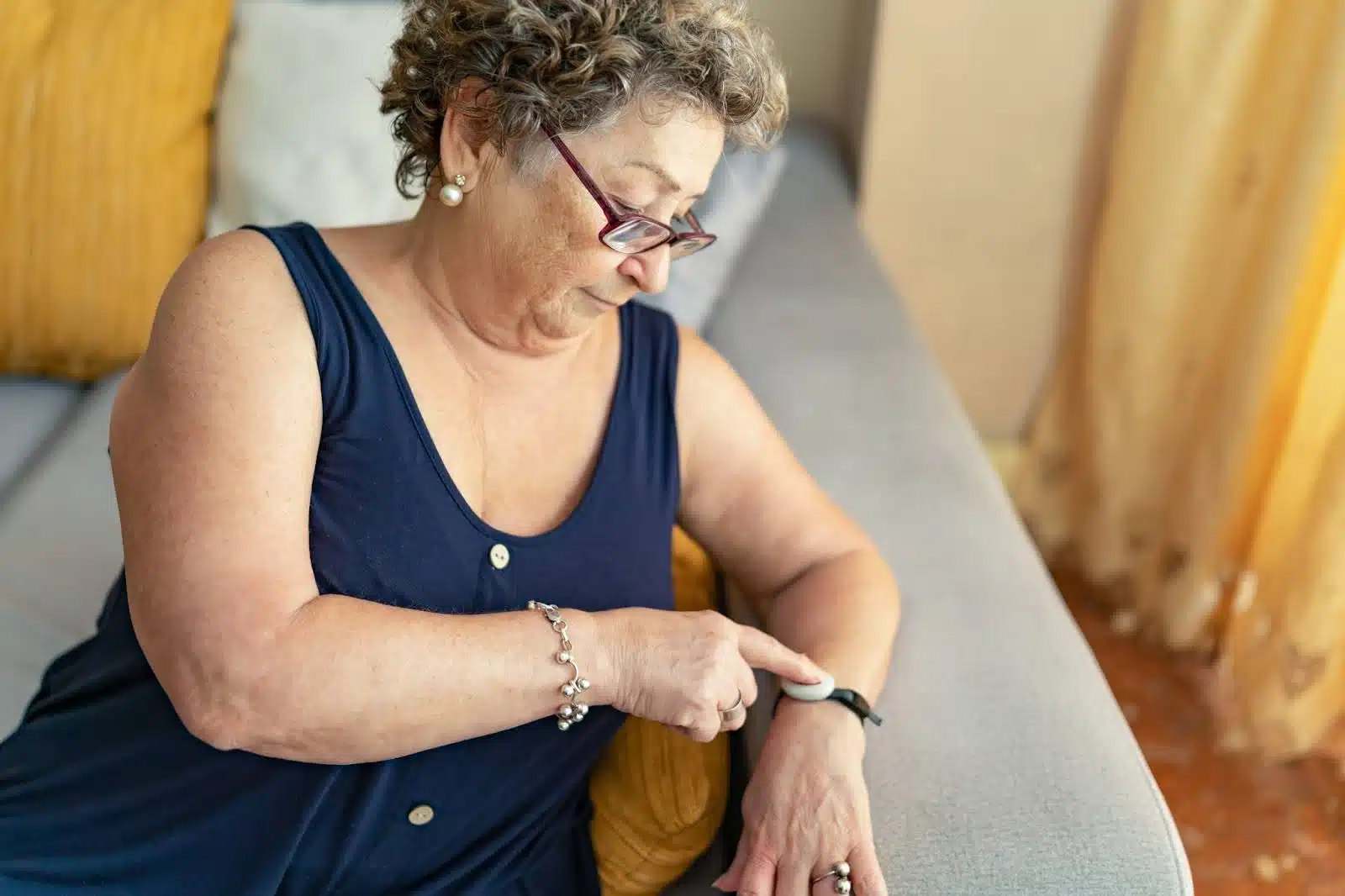 Older person with a life alert wristlet sitting on their couch.