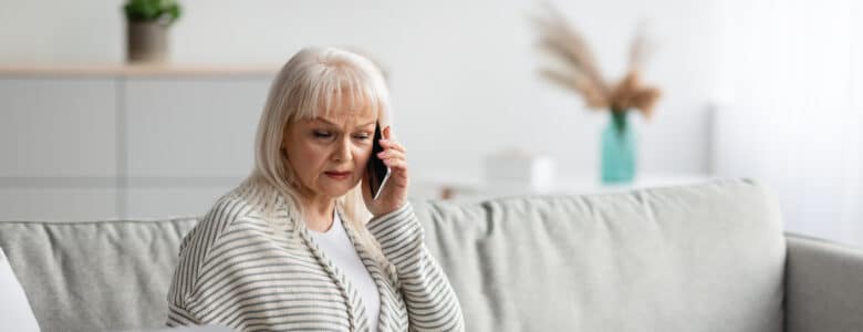Older woman sitting while on the phone and confused about a paper she is holding while looking at her laptop
