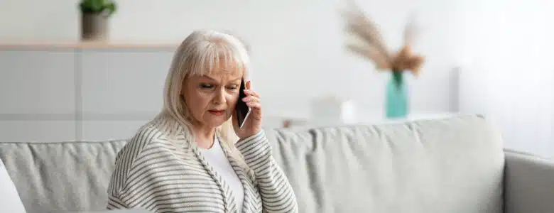 Older woman sitting while on the phone and confused about a paper she is holding while looking at her laptop