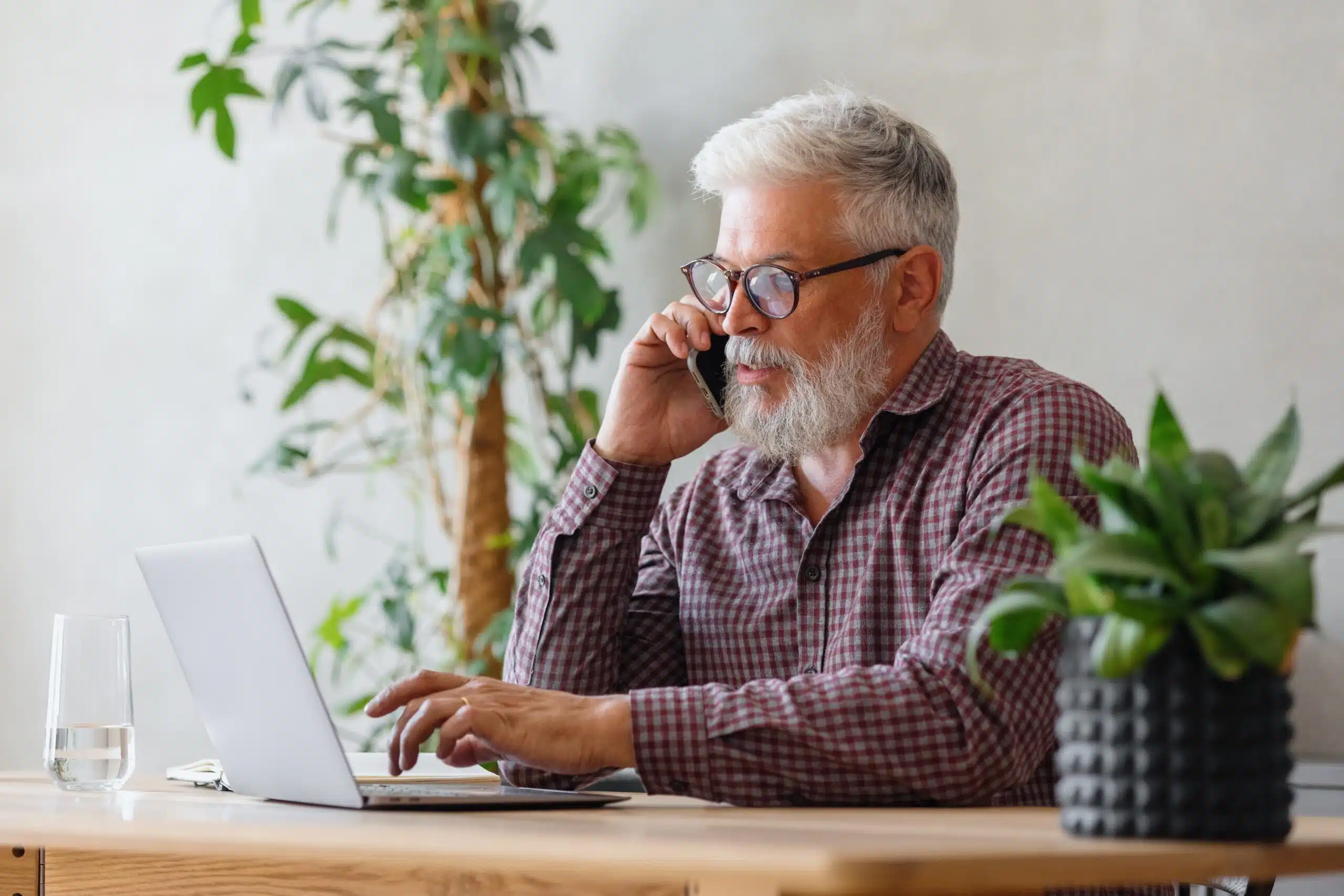 Older man on the phone while looking at his laptop.