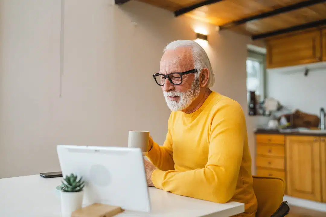 Senior drinking coffee while reading on their tablet